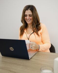 Jennifer Hume smiling at her laptop with a cup of coffee